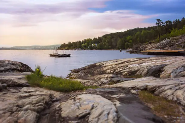 Beautiful Norwegian water scape with a rocky coast, boat, pine forest and blue sky at sunset