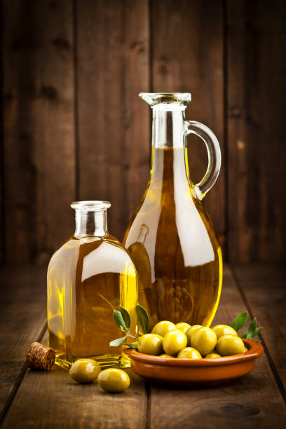 Olive oil and green olives Vertical shot of two olive oil bottles of different shapes and a brown bowl filled with green olives on rustic wood table. Predominant colors are gold, green and brown. DSRL studio photo taken with Canon EOS 5D Mk II and Canon EF 70-200mm f/2.8L IS II USM Telephoto Zoom Lens olive oil photos stock pictures, royalty-free photos & images