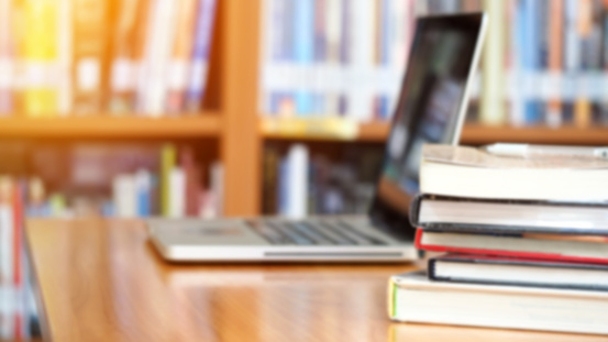 Book stack and laptop on workplace in library room with blurred focus for background, education concept