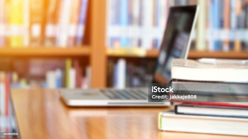 Business and education background Book stack and laptop on workplace in library room with blurred focus for background, education concept University Stock Photo