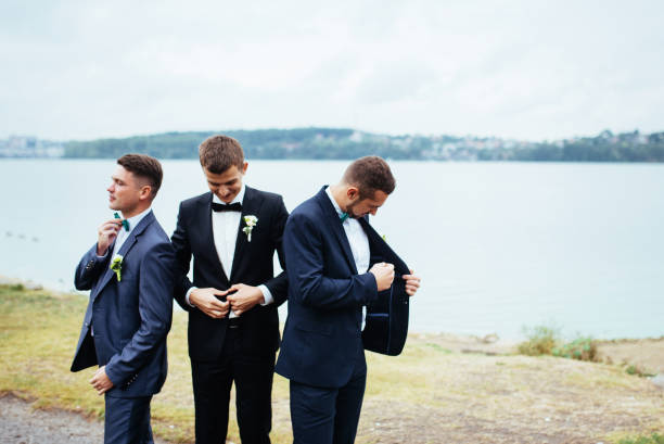 confident smiling handsome groom in black suit with two groomsma - wedding suit imagens e fotografias de stock