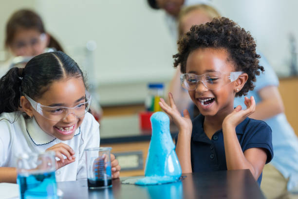 Excited African American schoolgirls enjoy science experiment Cute elementary STEM schoolgirls giggle as foam overflows beaker during science experiment. They are wearing protective glasses and school uniforms. independent school education stock pictures, royalty-free photos & images