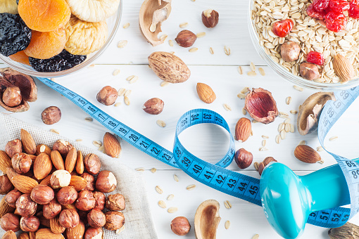 Healthy food. Ingredients for healthy breakfast on white wooden background with dumbbell and measuring tape. Oatmeal, dried cherry, apricots, figs and nuts, close up, top view. The concept of natural organic food.