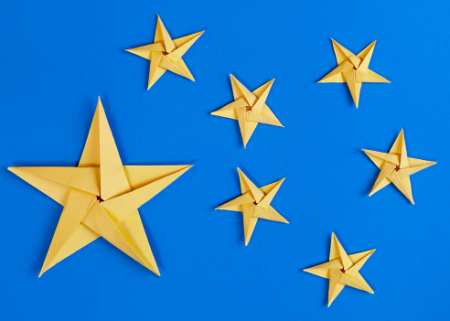 Group of large and small stars made from yellow card on a blue background and photographed from above.