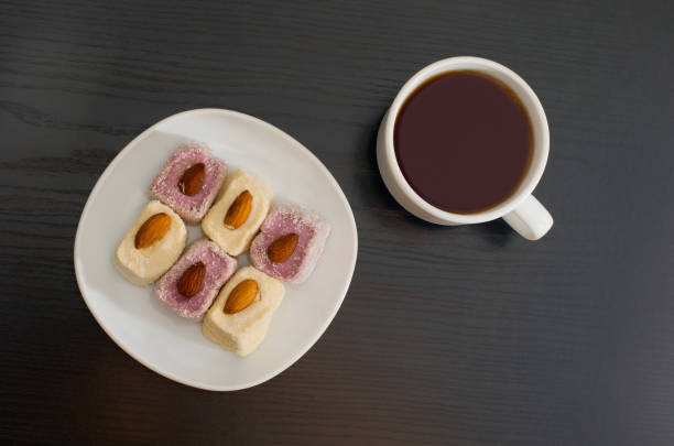 istock Mug of tea and Turkish Delight with almonds on a plate, top view, black background 644064282
