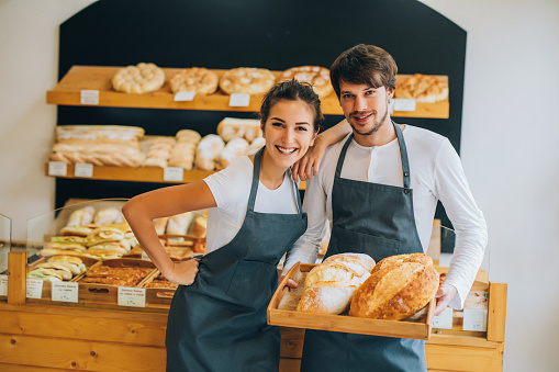 Two beautiful young bakers offering bread at the bakery.