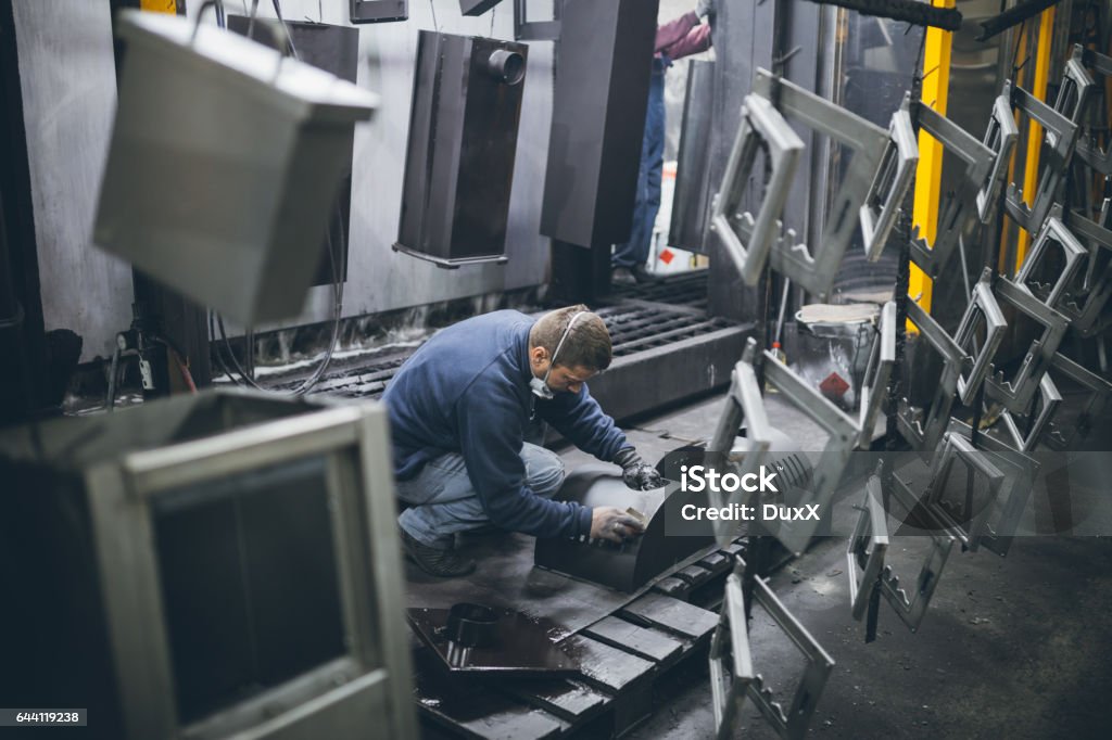 Metallurgy industry interiors Metallurgy industry. Factory for production of heavy pellet stoves and boilers. Manual worker painter on his job. Extremely dark conditions and visible noise. Focus on foreground. 30-39 Years Stock Photo