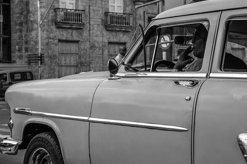 Havana, Cuba - March 19, 2016. Black and white photography of a man smoking inside  a  classic car. In the bottom, some windows and balconies of an old building.