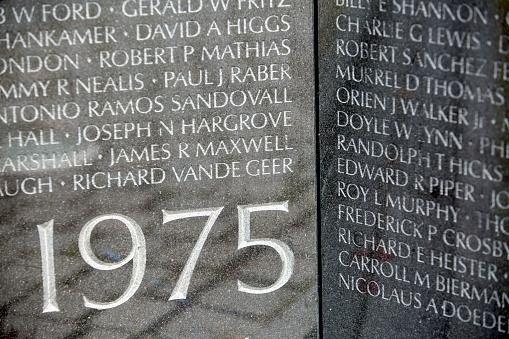 A close up  of the names of dead solidiers on the reflective black marble on the Vietnam Memorial on the Mall in Washington DC. Each name is in chronological order of their death. The Date of 1975 indicated the year the Vietnam war ended.