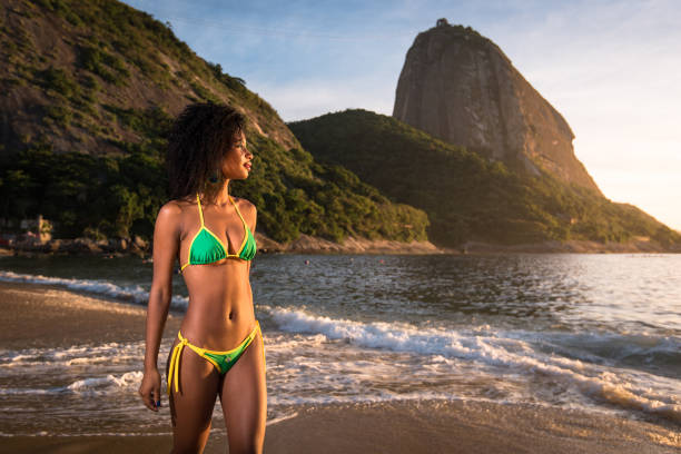 Beautiful Brazilian Girl Walking in the Beach Young Beautiful Brazilian Woman in Bikini Walking at the Beach by Sunrise With the Sugarloaf Mountain in the Background, in Rio de Janeiro black woman bathing suit stock pictures, royalty-free photos & images