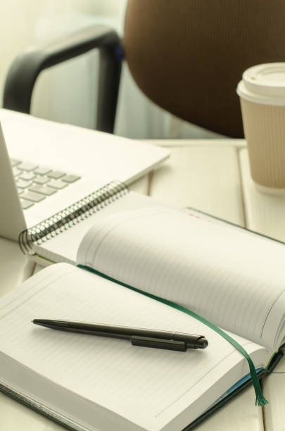 istock Open notepad with black pen on work-table. Paper cup of coffee, office stuff, laptop, copy space 644144344