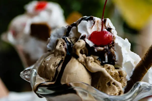 Chocolate ice cream sundae dessert topped with whipped cream, chocolate sauce and cherry.