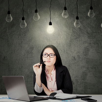 Portrait of young businesswoman thinking solution while sitting with light bulb over her head