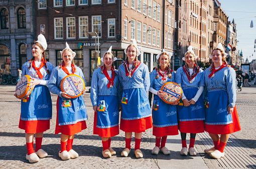 Smiling women in traditional Dutch costumes with gouda cheese truckles at Gouda Cheese Market in Amsterdam, Netherlands