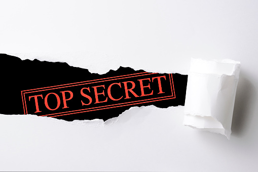 Looked into through the tearing white color paper, against “TOP SECRET” rubber stamp, isolated on black.