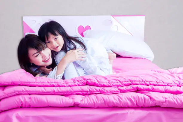 Portrait of happy mother and child lying on the bed while playing together on the bedroom