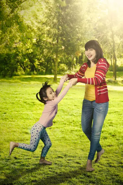 Photo of a pretty young mother and her little daughter playing together at the park while holding hands