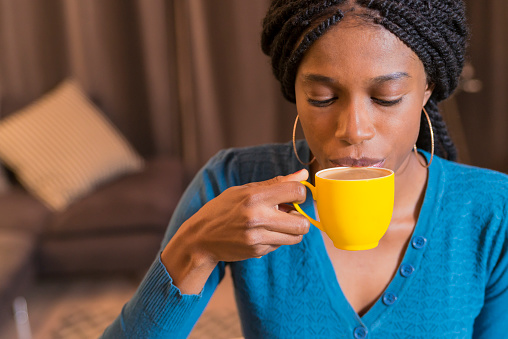 Beautiful young African woman enjoying a cup of coffee while relaxing at home