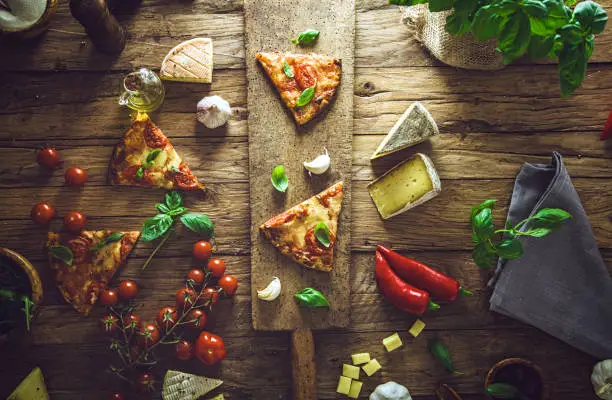 Pizza slice on wood with ingredients. Pizza with cheese, tomatoes and basil. Rustic italian pizza