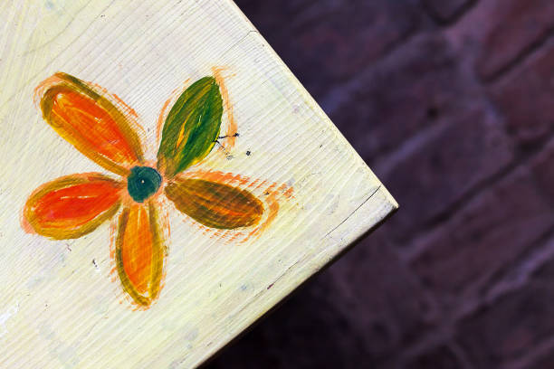 Details of an old wooden table with painted flower on it, brick floor in blurry background.
