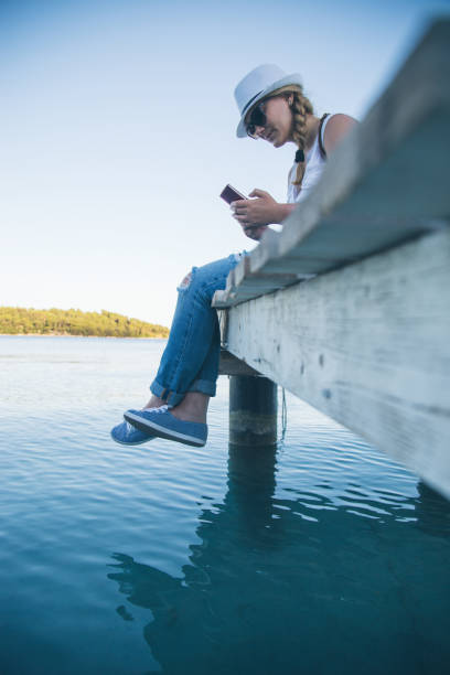 istock Girl with smartphone sitting at the pier 644288086