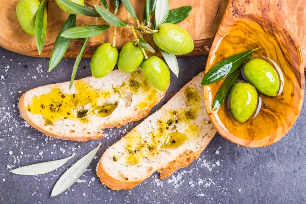 Olive oil and bread, fresh olives branch directly above, tasting extra virgin olive oil.