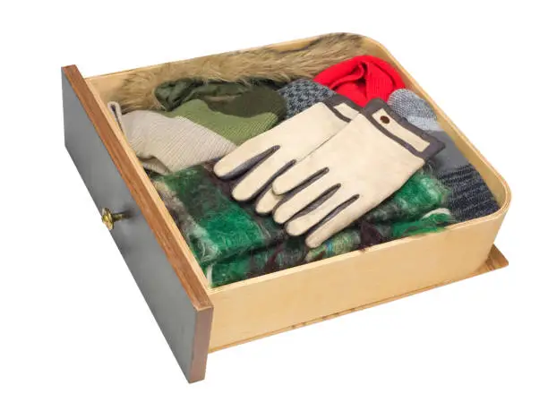 Wooden drawer of a dresser with warm winter clothes - gloves, scarf,  cap, fur collar. Isolated with patch