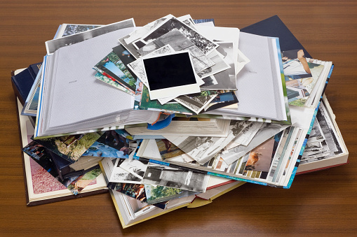 Nostalgia by youth - old family photo albums and photos lie a heap on a wooden table.