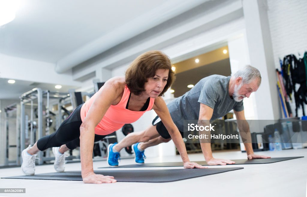 Senior couple in gym working out, doing push ups Beautiful fit senior couple in gym working out, doing push ups. Push-ups Stock Photo