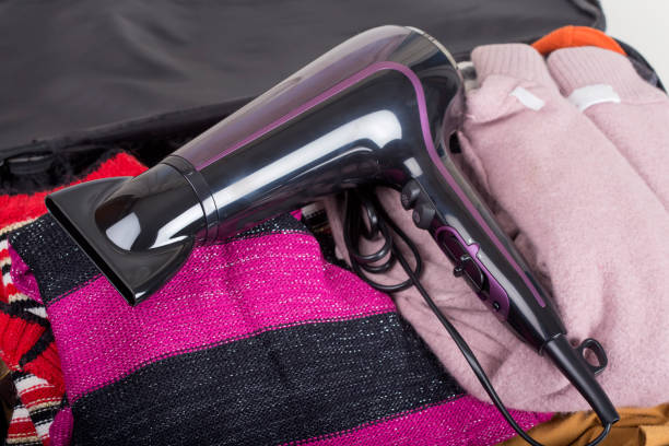 Modern hair dryer on travel bag with clothes