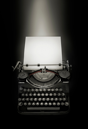 Vintage typewriter against black  background. Low key edition of an ancient typewriter integrated on black background to give prominence to the space for text at the white page. Light effect over copy space