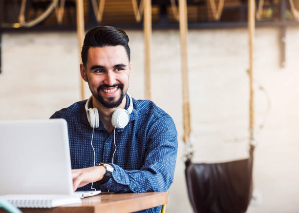 istock Cheerful Young Man Using Tablet with Earphones In Coffee Shop 644512448