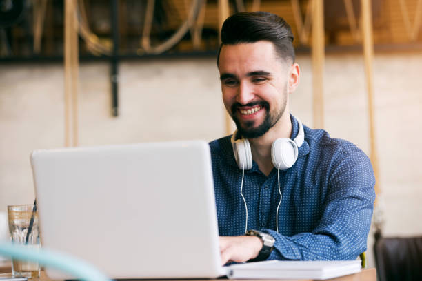 istock Cheerful Young Man Using Tablet with Earphones In Coffee Shop 644513974