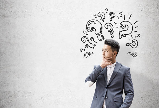 istock Asian businessman, question marks, concrete wall 644545346