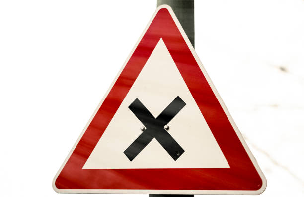 German road sign, triangular with a red border and a black cross in the middle on white background.