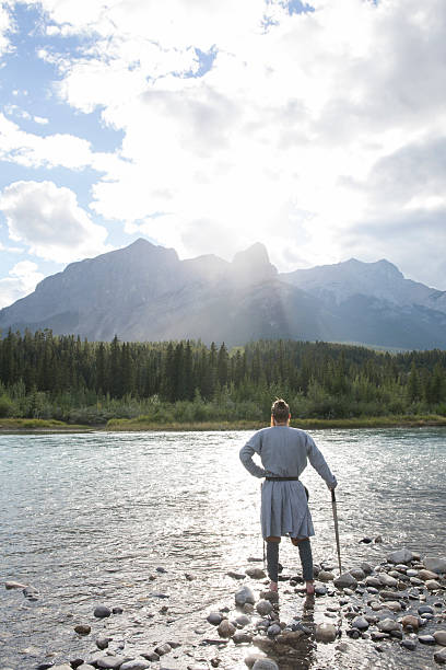 hombre vestido con traje vikingo se encuentra en la orilla del río - 20s standing one man only sword fotografías e imágenes de stock