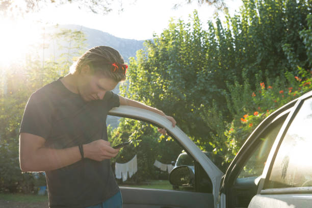istock Young man leans on car and sends text message 644596143