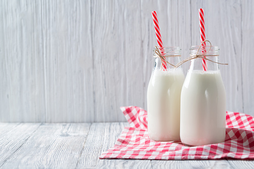 Bottles of milk with red straws and checkered towel on grey wooden background