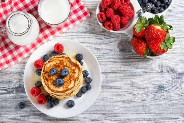 pila de panqueques con arándanos frescos, frambuesas y miel, leche y bayas frescas, concepto de desayuno saludable, vista superior - pancake buttermilk buttermilk pancakes equipment fotografías e imágenes de stock