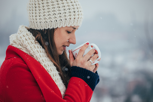 One woman, winter day, relaxing outdoors, holding tea cup.