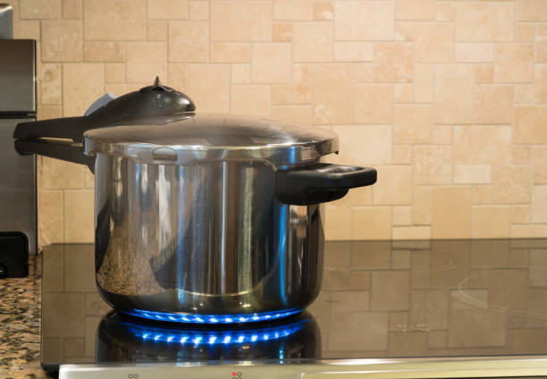 Stainless steel pressure cooker on hob Stainless steel pressure cooker letting off steam on a modern induction cooking hob with glass top environmental pressure oven photos stock pictures, royalty-free photos & images