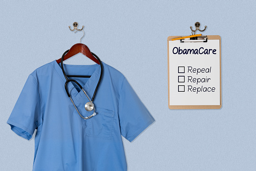 Blue medical scrubs uniform shirt hanging on a hanger with stethoscope with Obamacare options on clipboard