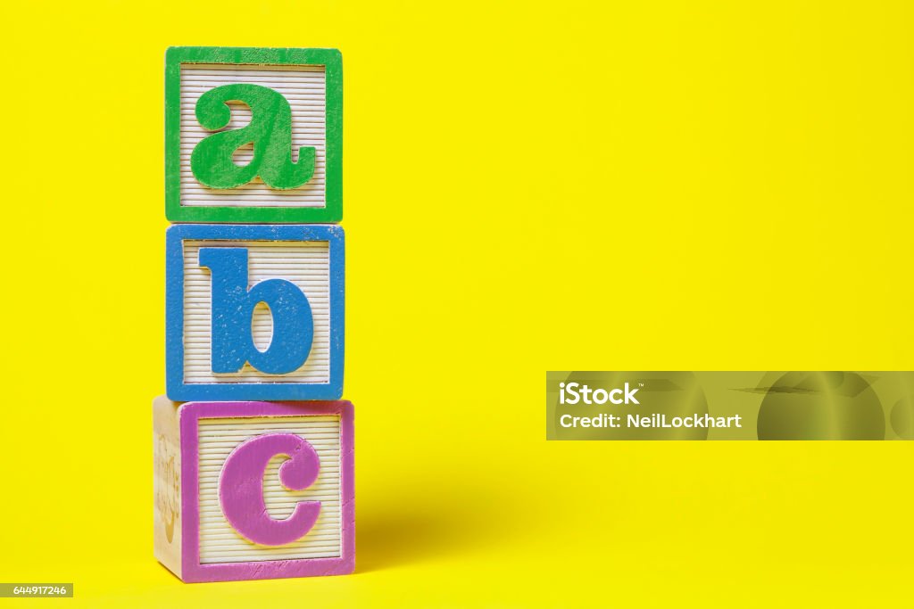 ABC Alphabet blocks stacked up on yellow background Toy Block Stock Photo