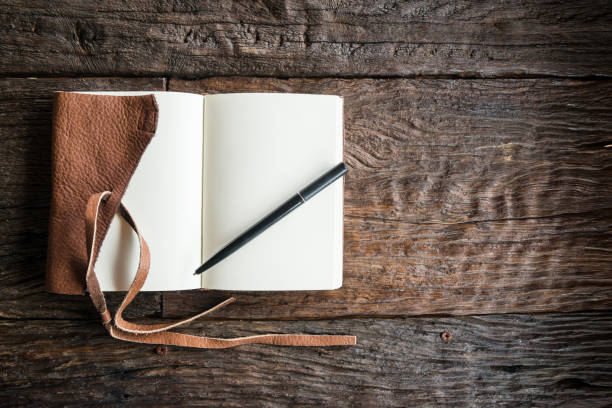 The leather book with pen on the wood table.