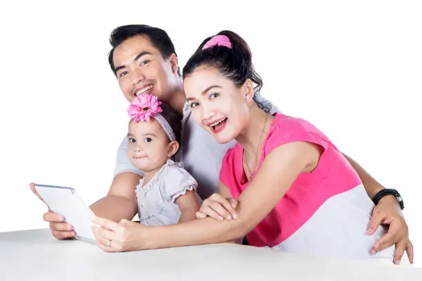 Portrait of happy family using digital tablet while smiling at the camera, isolated on white background