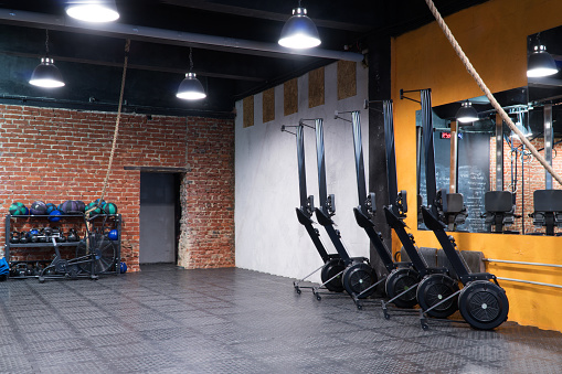 Modern fitness gym with a row of rowing machines and sport equipment at the wall