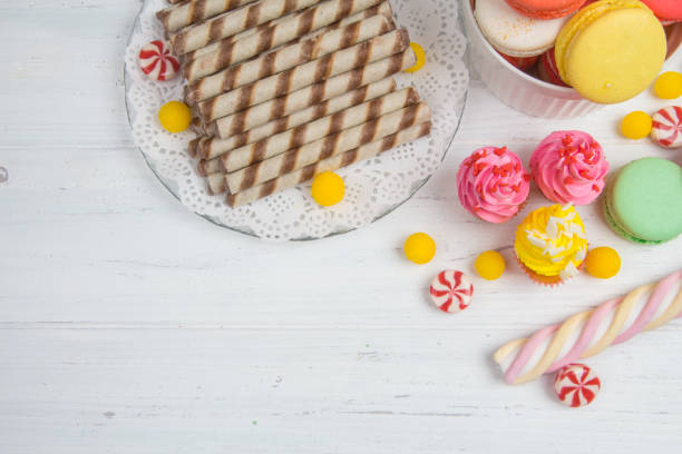 istock Wafer rolls, colored candies, cupcakes and macaroons on wooden background. 644969724