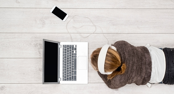 Top view header image of girl using laptop and mobile phone on floor with headset to stream music or movie