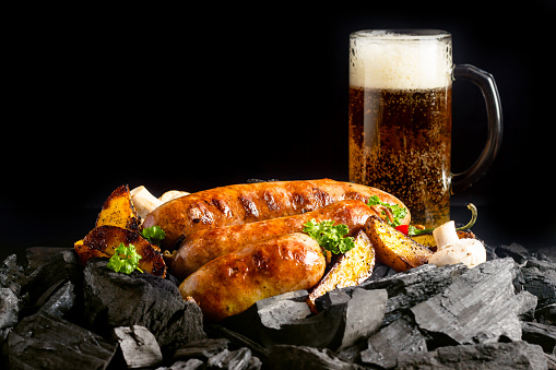 Sausages grilled over charcoal with a beer in the background