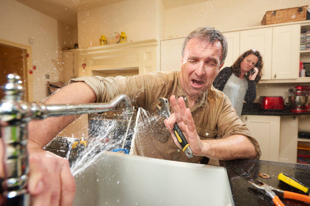 plumbing mishap give it a go DIY hero tries his hand at fixing the tap . His wife is already on the phone to an emergency plumber as water gushes from the broken tap kitchen sink photos stock pictures, royalty-free photos & images